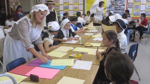 Photos by Misty DUPLESSIS Colonial dressed parent Sharon Vinceri explains how to do the cross stitch art. Valley View Students Adopt Colonial Ways