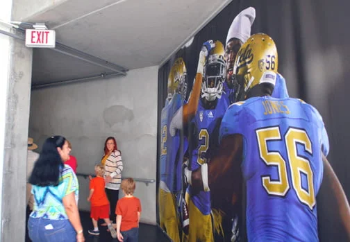 Guests pass by a mural of UCLA football players located outside the Bruins locker room during the first ever group tours of the Rose Bowl.